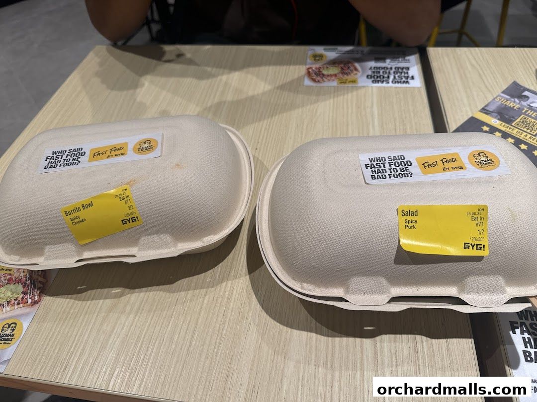 Two takeaway food containers from Guzman y Gomez, one burrito bowl and one salad, on a table.