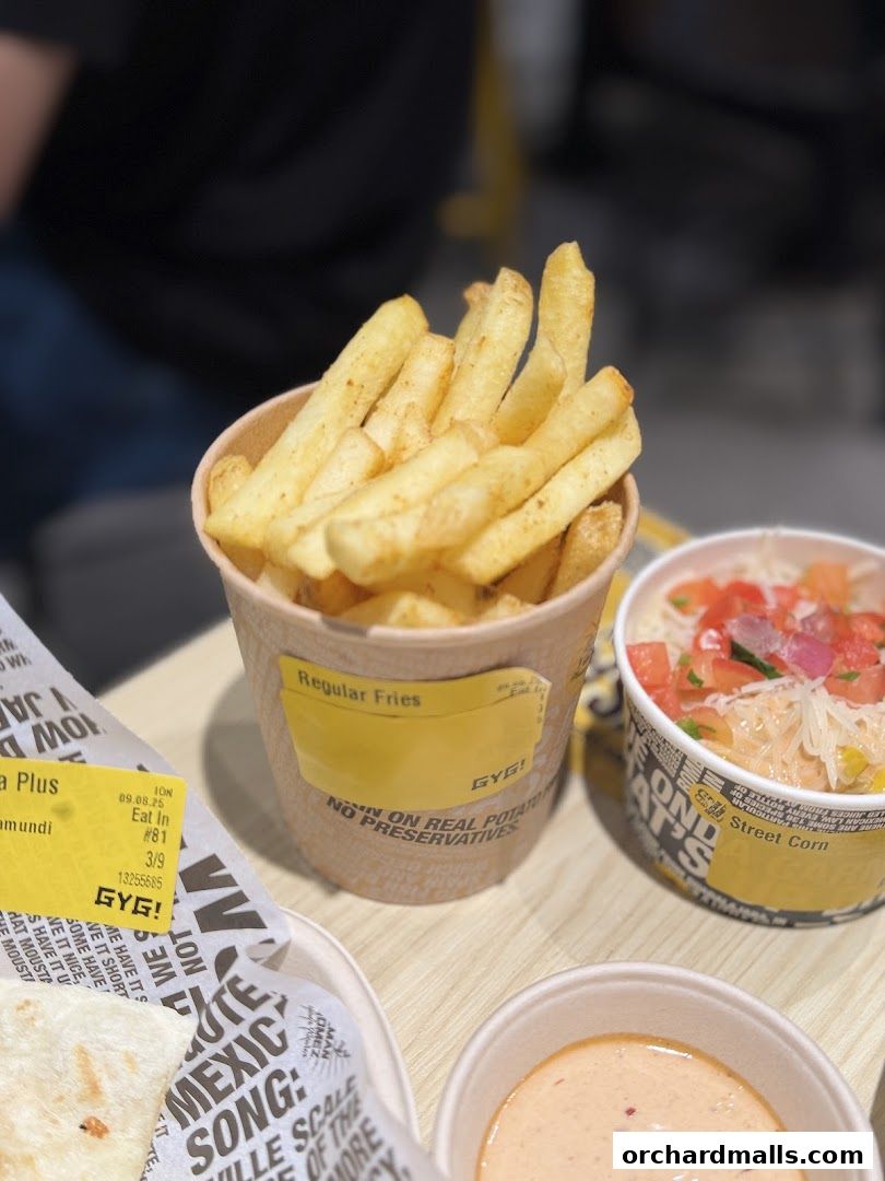 A close-up of a cup of regular fries from Guzman y Gomez, with street corn and dipping sauce visible.