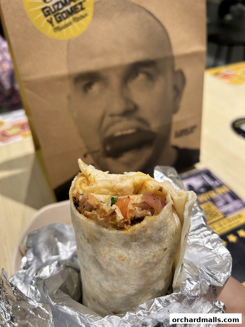 A close-up of a delicious burrito from Guzman y Gomez, with a branded bag in the background.