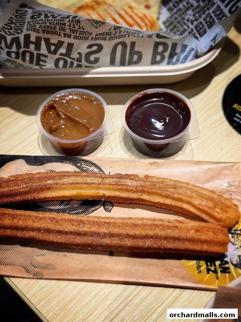 Two churros served with caramel and chocolate dipping sauces.