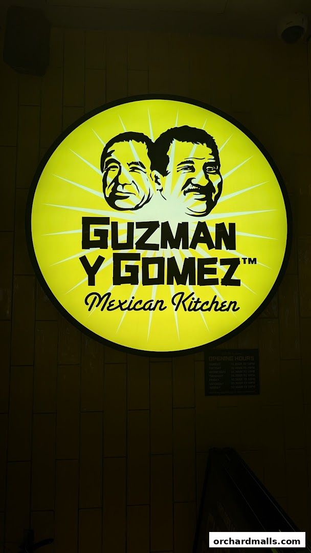 A bright yellow circular sign for Guzman y Gomez Mexican Kitchen with two cartoon faces.