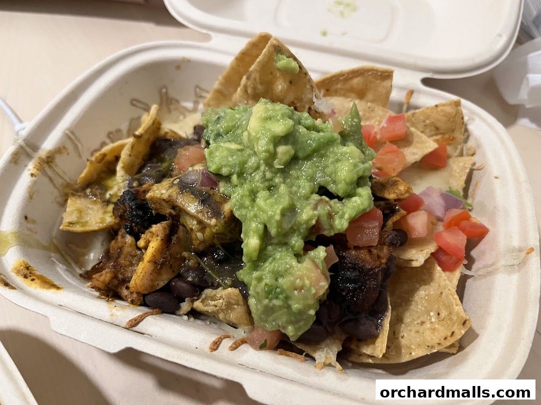 A close-up of a takeaway container filled with nachos, chicken, beans, guacamole, and salsa.
