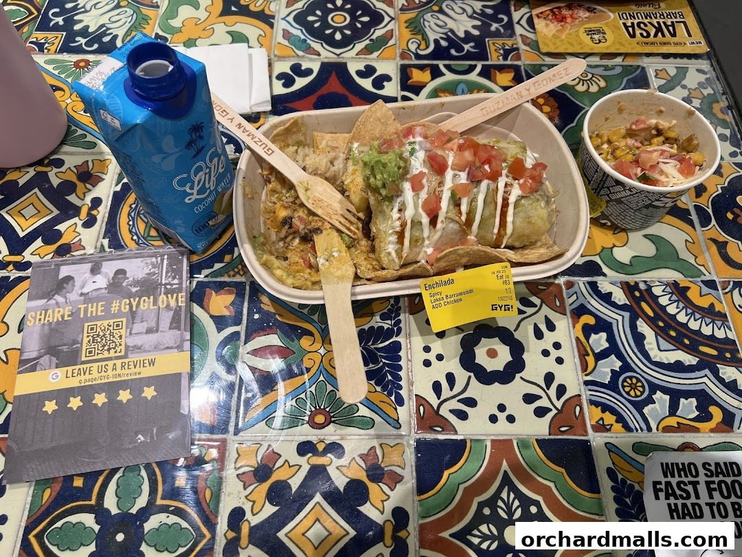 A table with Guzman y Gomez food, including an enchilada and a side of corn salsa, with a coconut water drink.