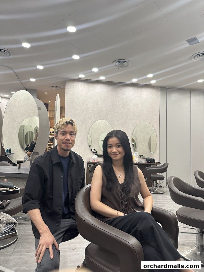 A male hairstylist and a female client pose for a photo inside a modern hair salon.