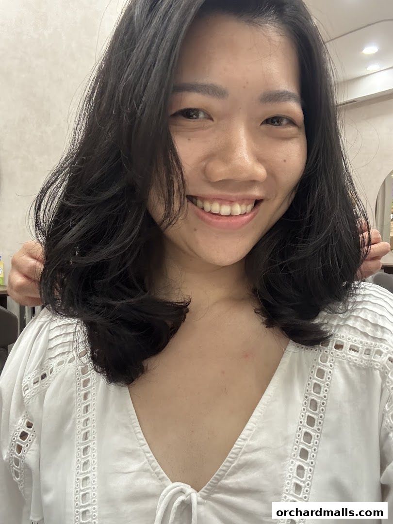 A smiling woman with dark, layered hair and a white top.