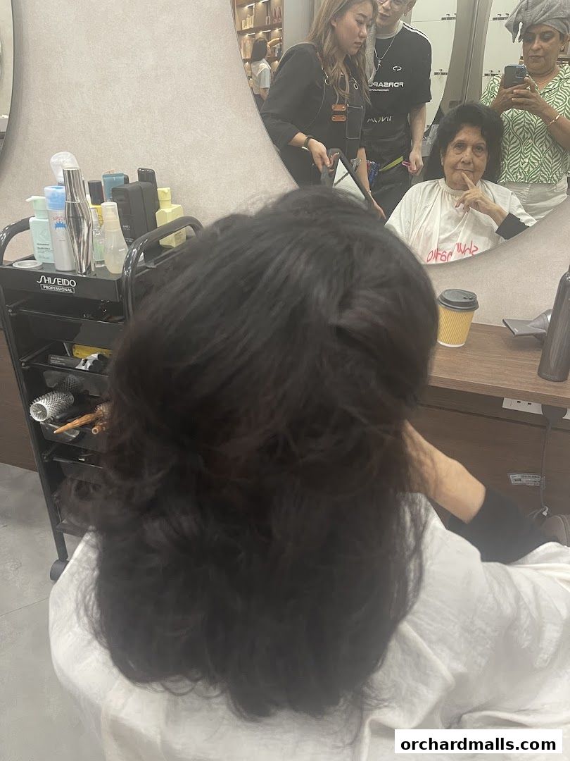 A client sits in a salon chair, getting their hair styled by professionals.