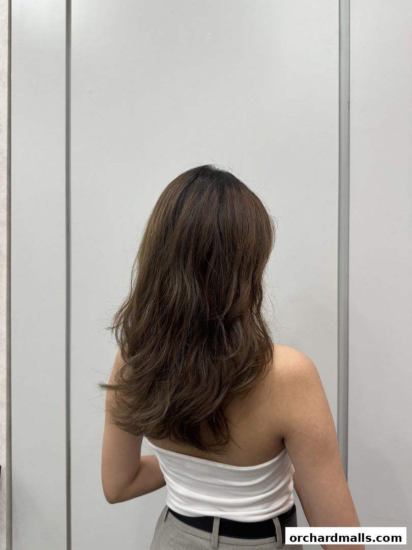 A person with long, wavy brown hair styled with subtle highlights, viewed from the back.