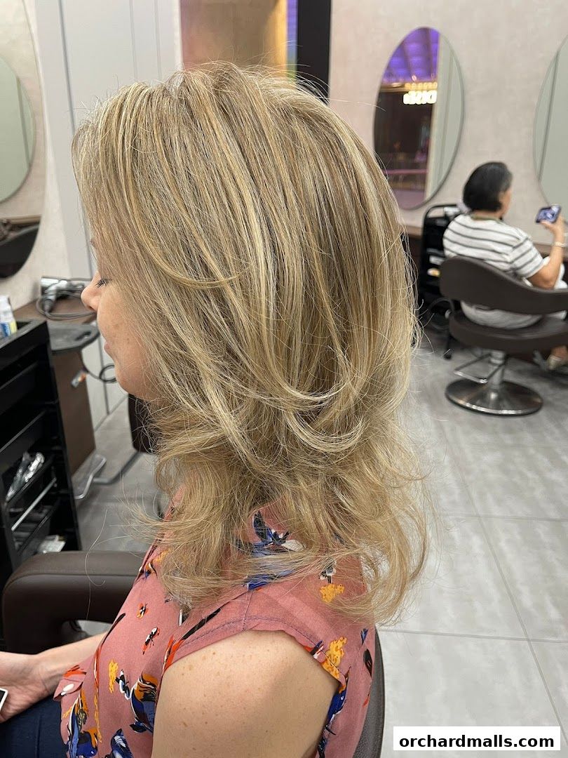 A woman with blonde, layered hair sits in a salon chair, showcasing a stylish haircut.