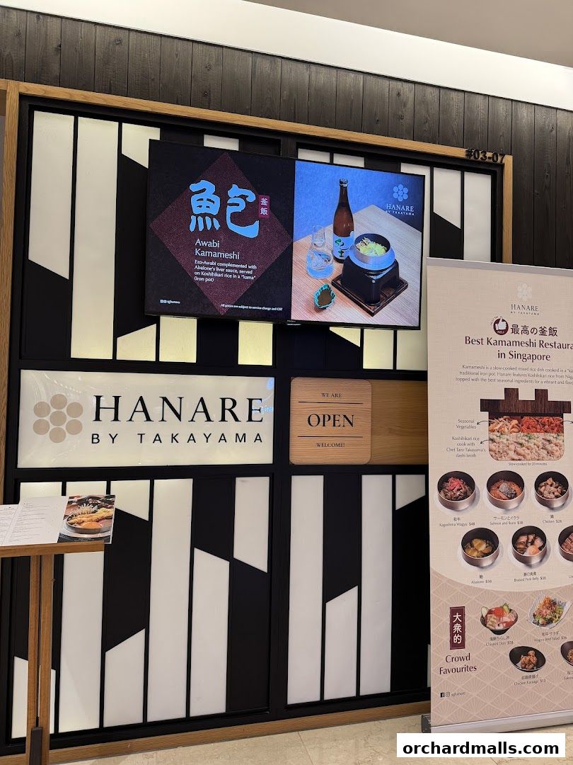 The entrance of Hanare by Takayama, a Japanese restaurant, with a digital display and a promotional banner.