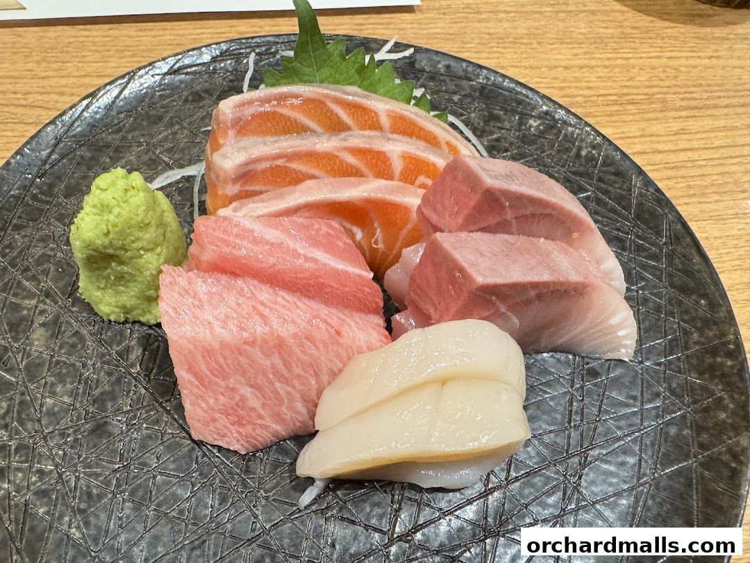 A plate of assorted sashimi, including salmon, tuna, and scallop, with a side of wasabi.