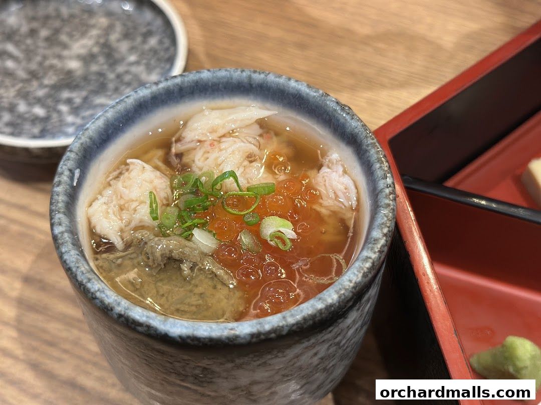 A close-up of a Japanese dish with crab meat, roe, and broth in a ceramic bowl.