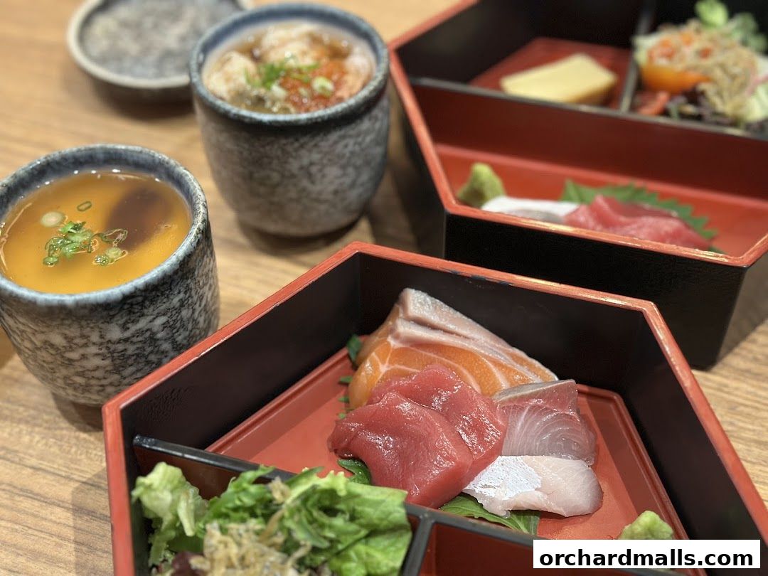 A close-up of a Japanese bento box with sashimi and soup, garnished with green onions.