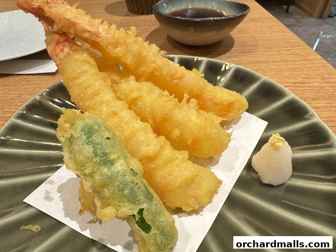 A plate of crispy tempura shrimp and vegetables served with dipping sauce.