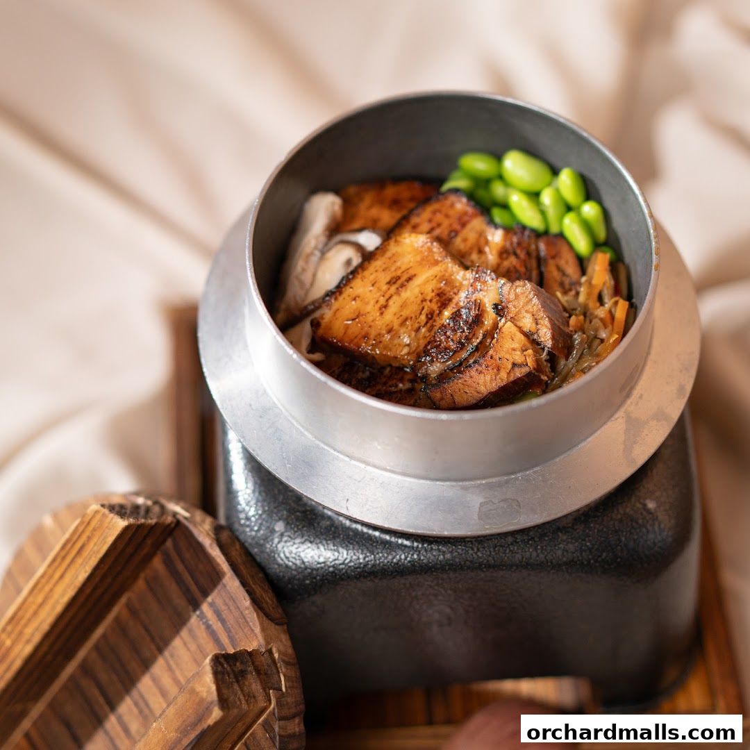 A close-up of a Japanese kamameshi dish with grilled meat and edamame.