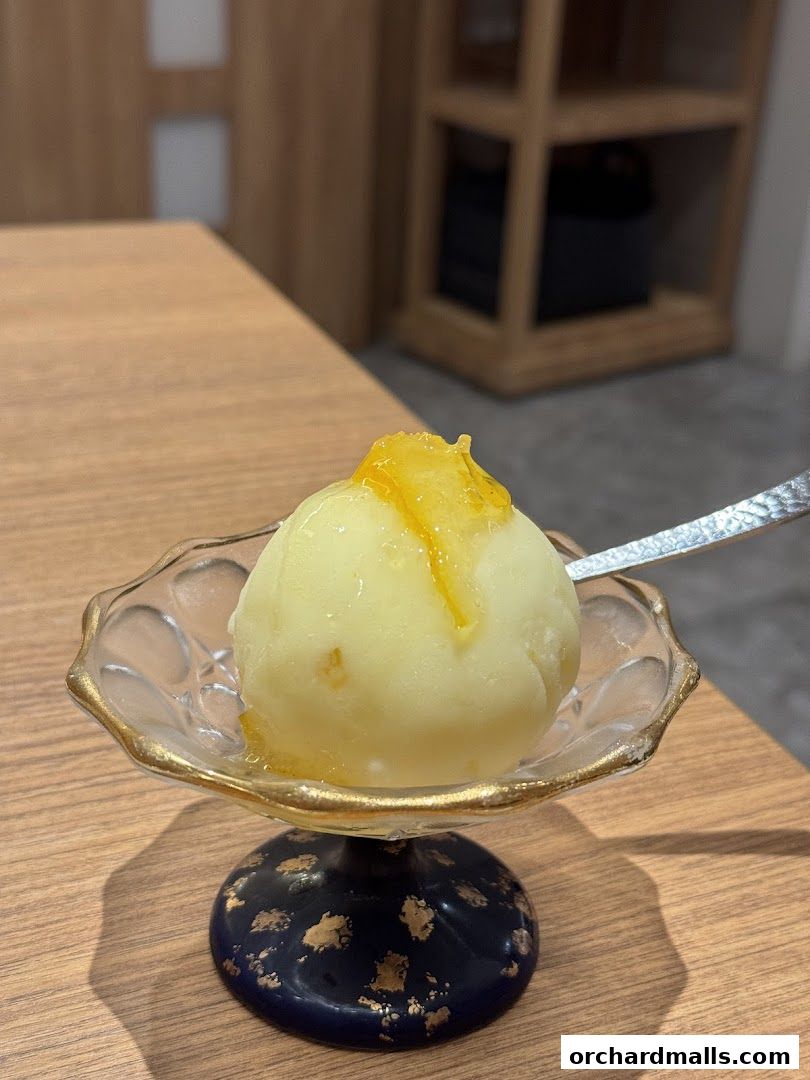 A scoop of pale yellow ice cream with a citrus topping in an ornate glass dish.