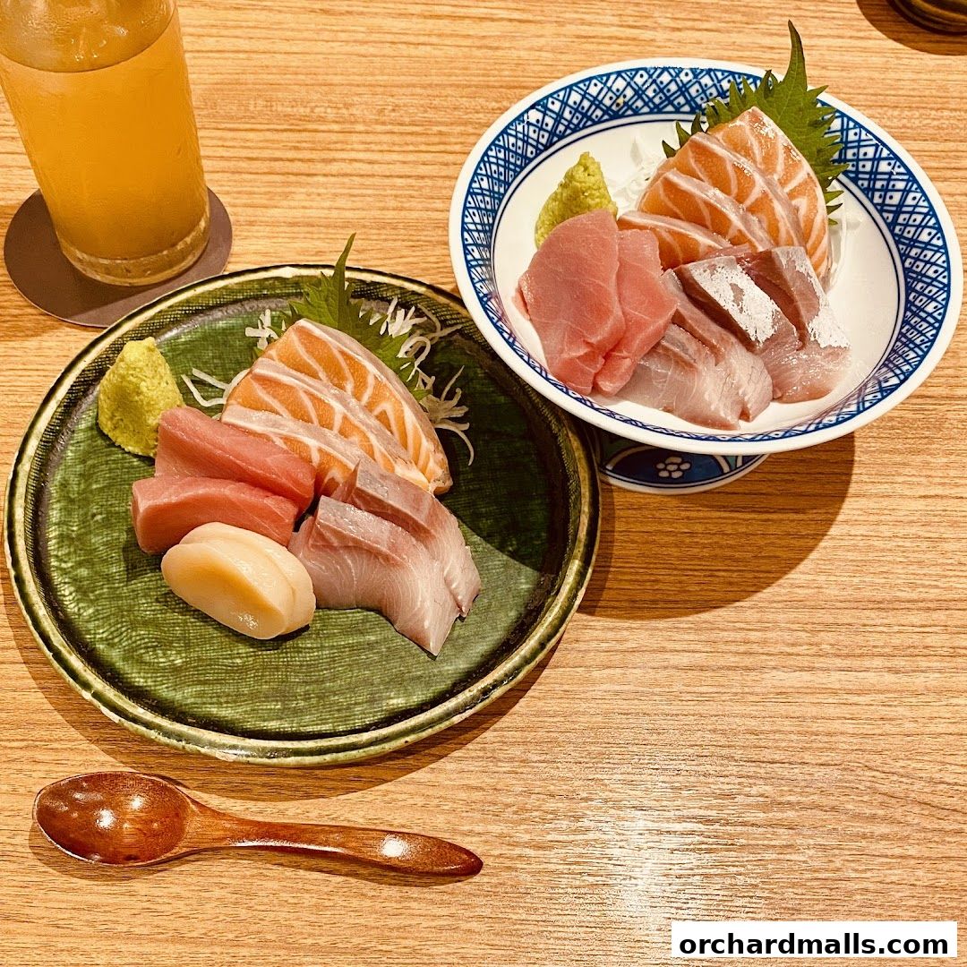 Two plates of fresh sashimi, a glass of drink, and a wooden spoon on a wooden table.