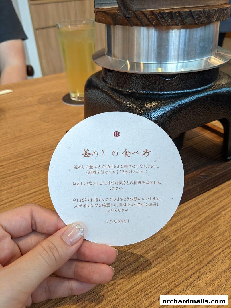 A hand holds a circular card with instructions on how to eat Kamameshi.