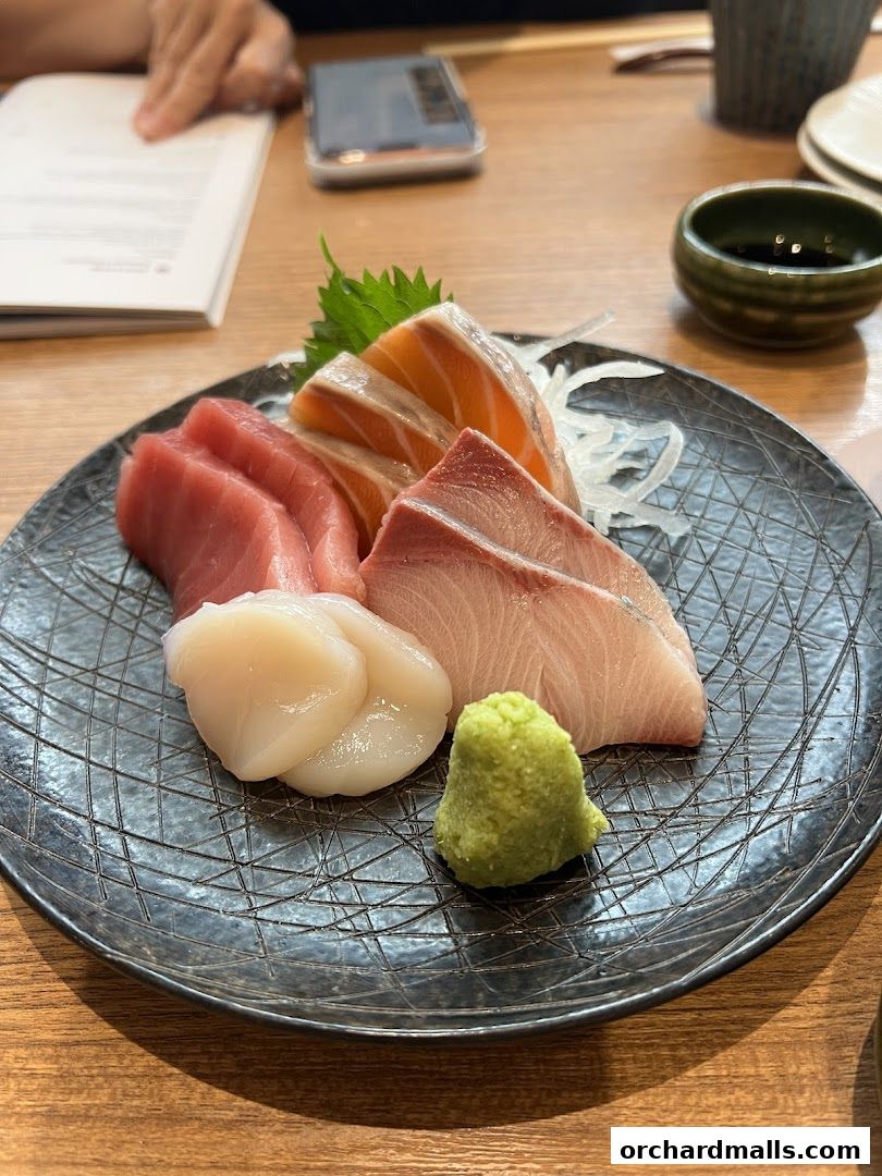 A plate of fresh sashimi with tuna, salmon, hamachi, and scallops, served with wasabi.