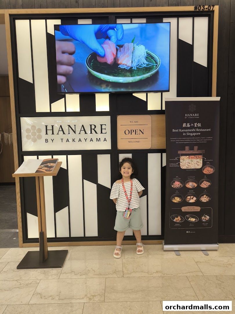 A child stands in front of the Hanare by Takayama restaurant entrance with a promotional banner.