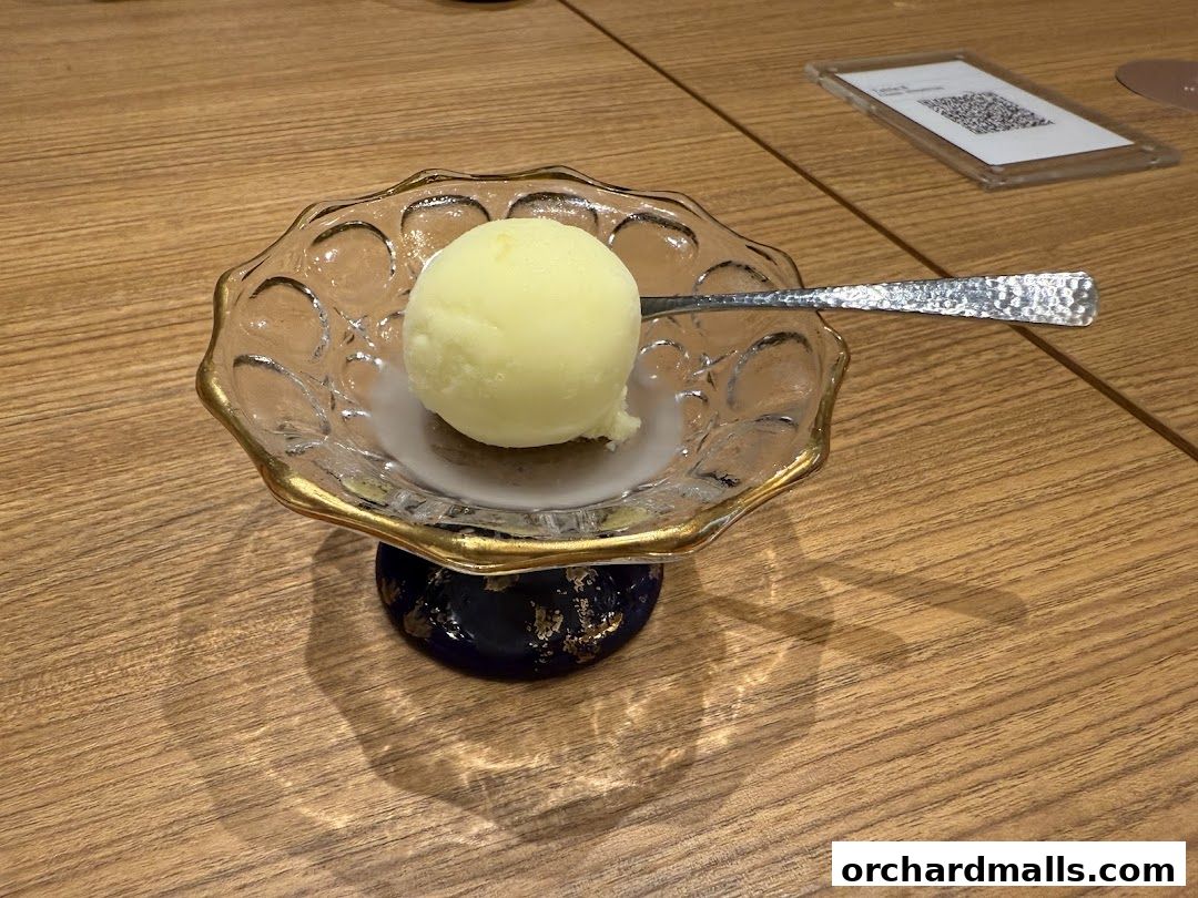 A single scoop of pale yellow ice cream served in an ornate glass bowl with a spoon.