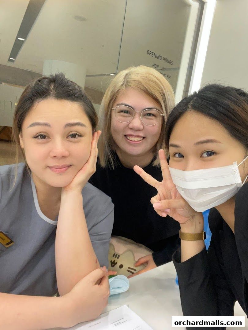 Three smiling women pose for a selfie in front of a shop with opening hours visible.