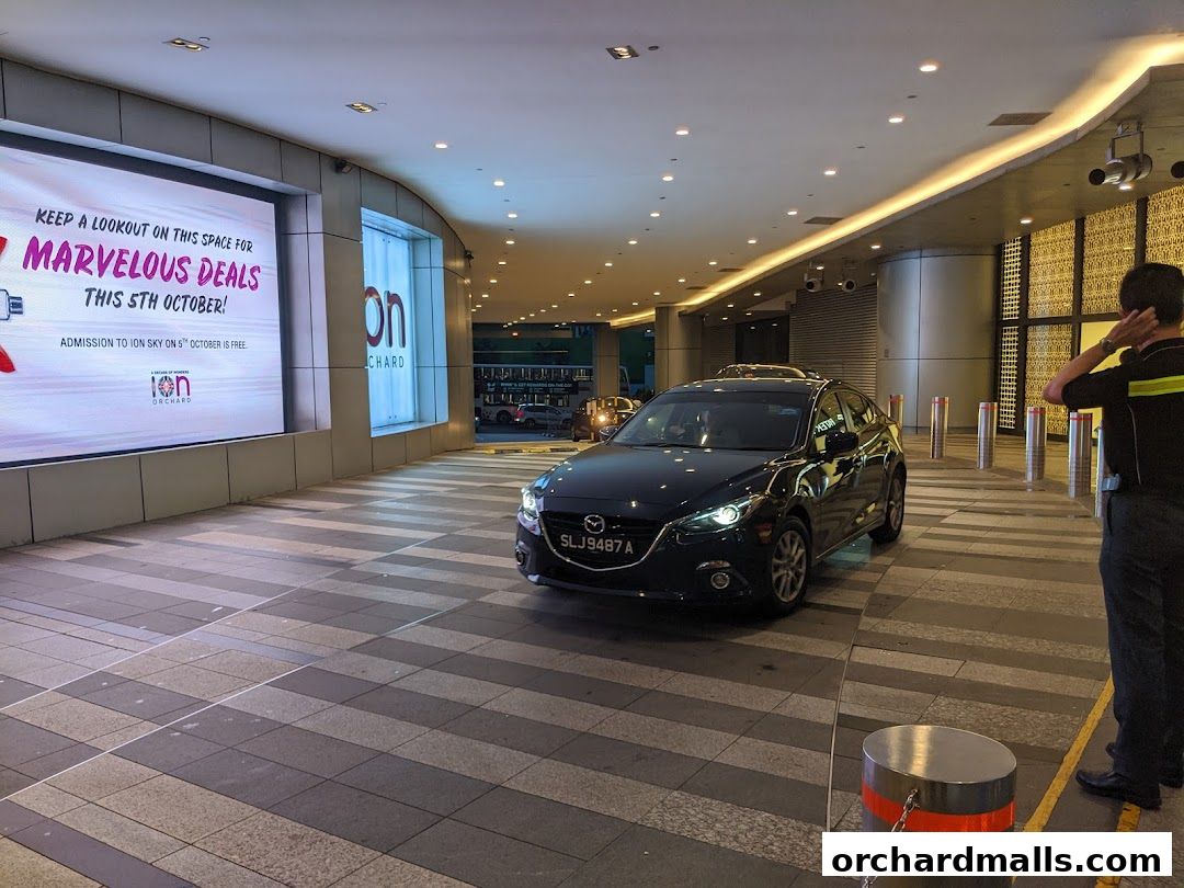 A car waits at the entrance of a building with a large digital billboard advertising deals.