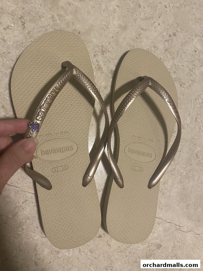 A pair of beige Havaianas flip-flops with metallic straps and a small charm.