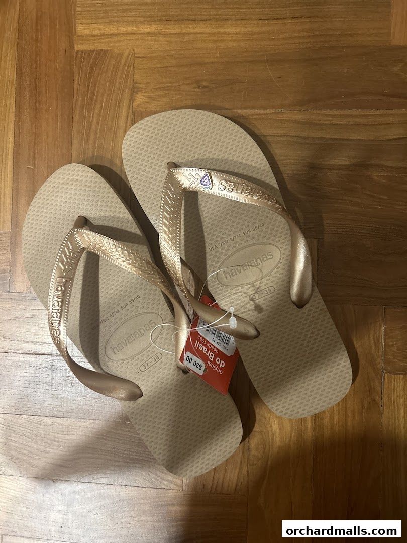 A pair of gold Havaianas flip-flops with price tags on a wooden floor.