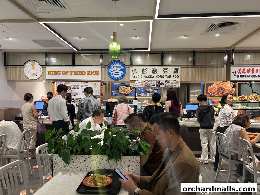 People ordering food at a busy food court with multiple stalls visible.