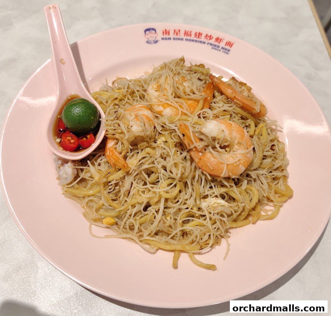 A plate of Hokkien Fried Mee with prawns, served with lime and chili on a spoon.