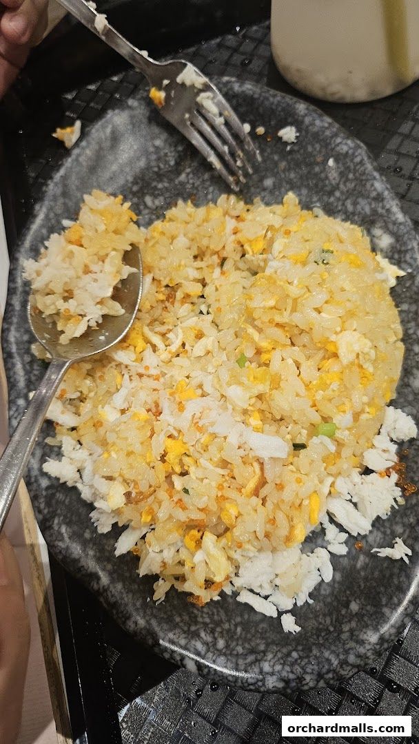 A close-up shot of a plate of crab fried rice with a fork and spoon.
