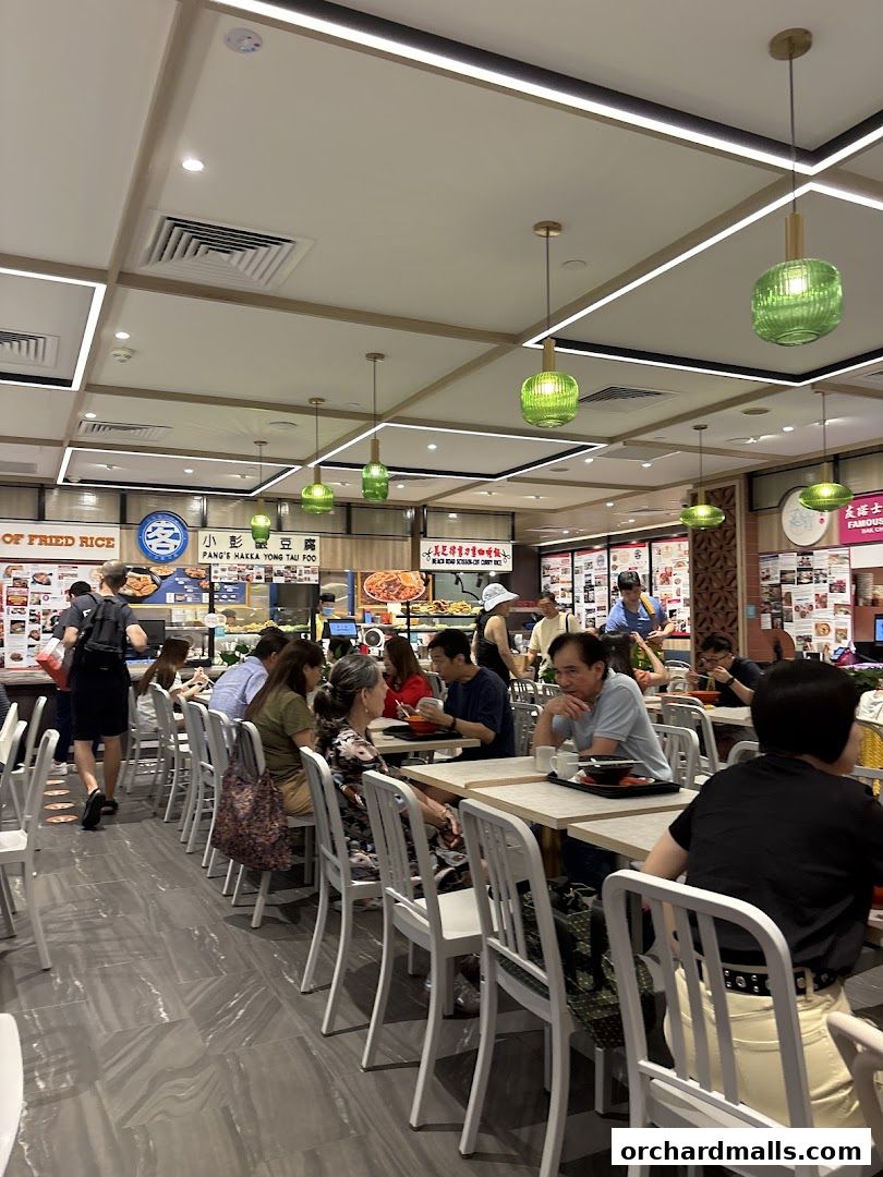 People dining at tables in a brightly lit food court with green pendant lights.