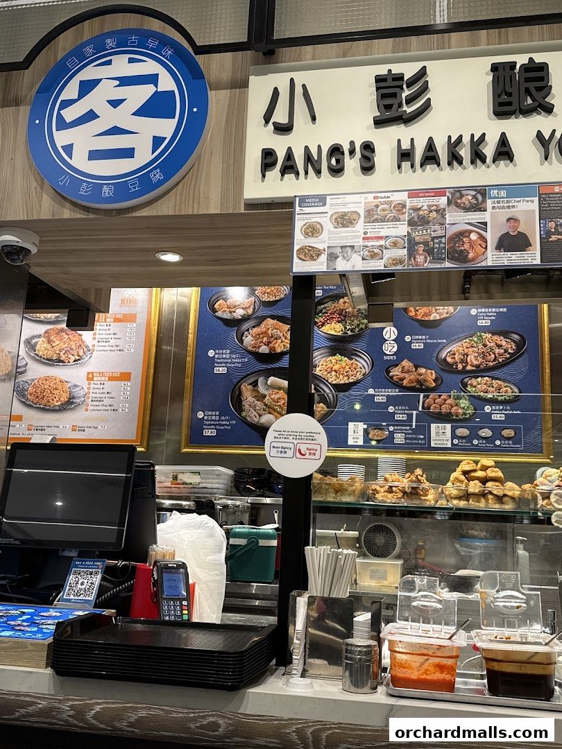 A food stall counter with a menu board displaying Hakka dishes and various condiments.