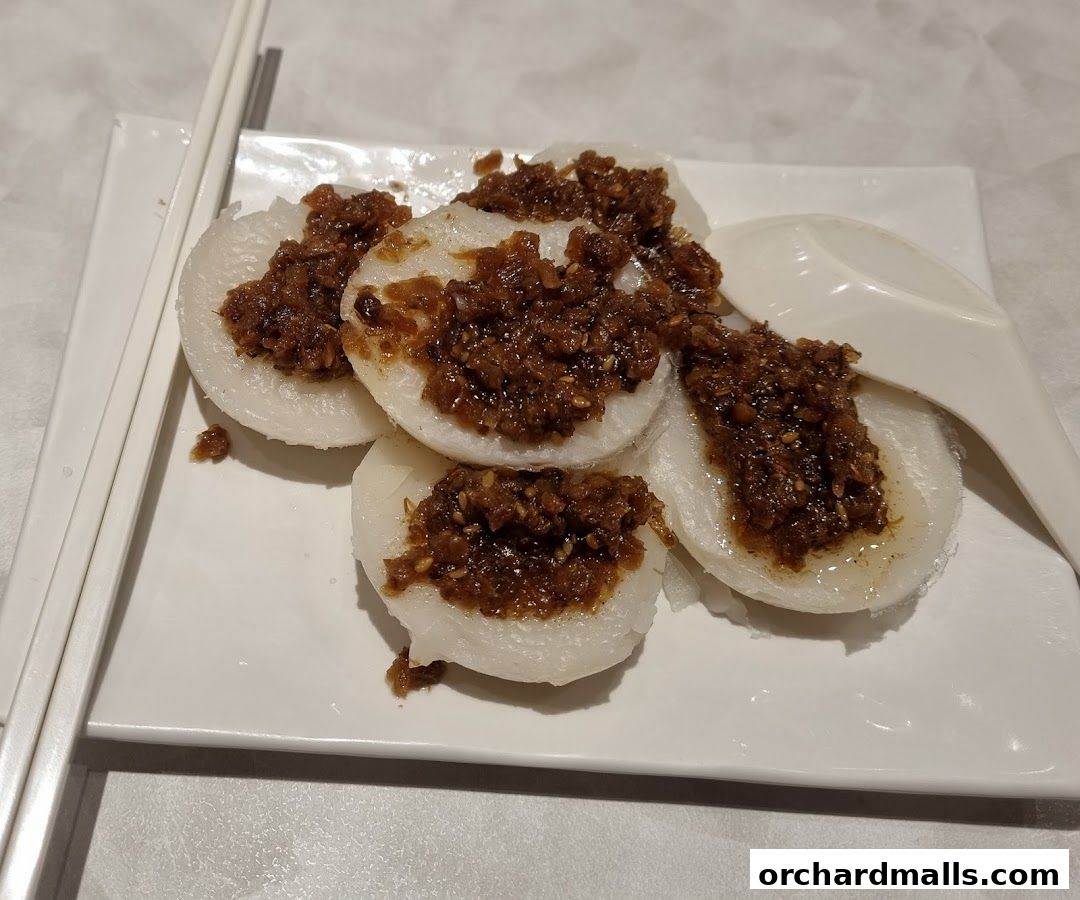 A plate of white rice cakes topped with a savory brown sauce and sesame seeds.