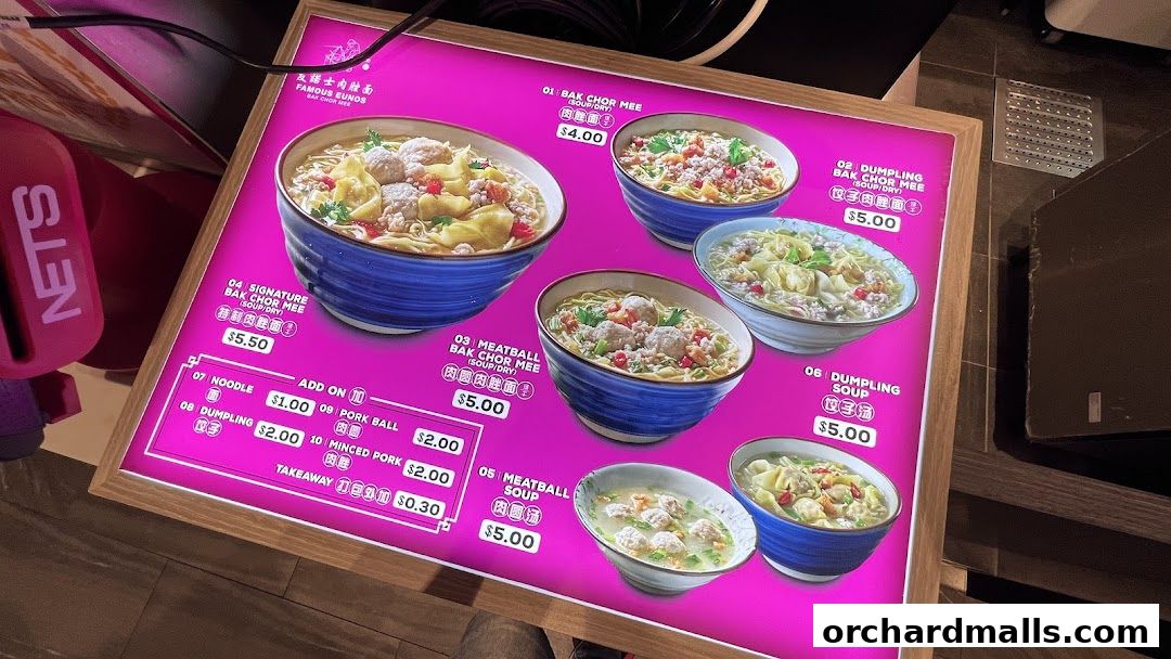 A brightly lit menu board displaying various noodle and soup dishes with prices.