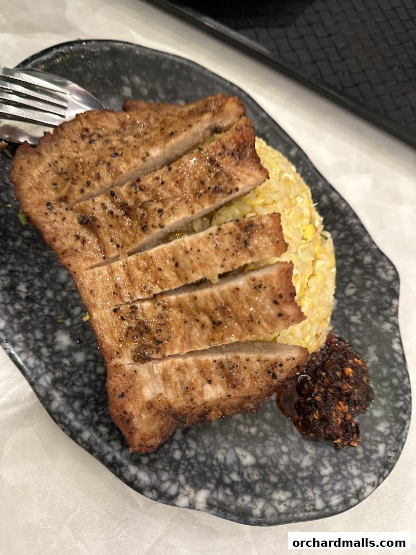 A plate of sliced grilled pork chop with fried rice and chili paste.