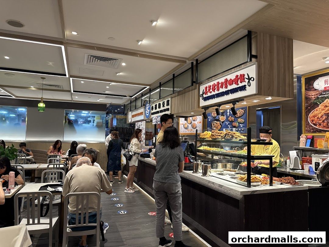 Customers ordering food at a busy hawker stall with a display of various dishes.