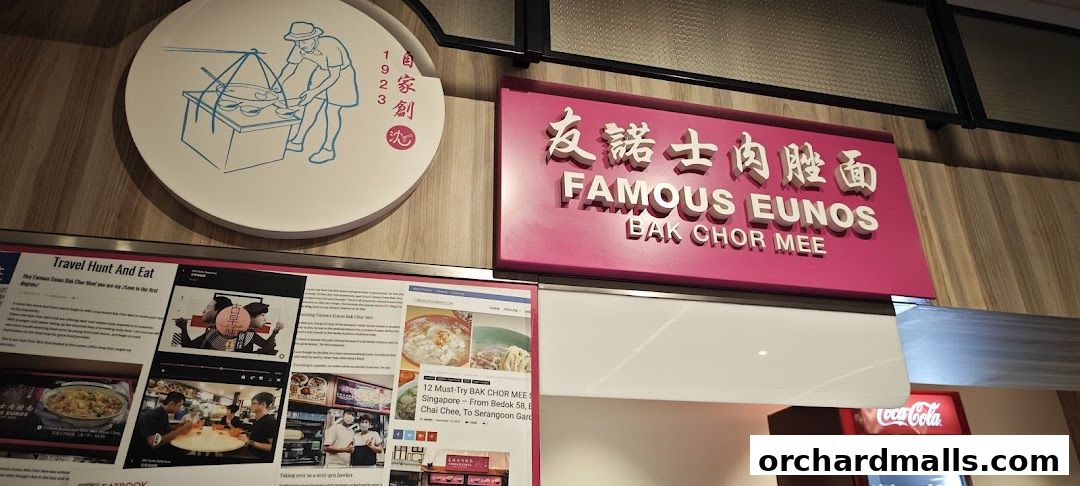 A shop sign for Famous Eunos Bak Chor Mee with a circular logo and newspaper clippings.