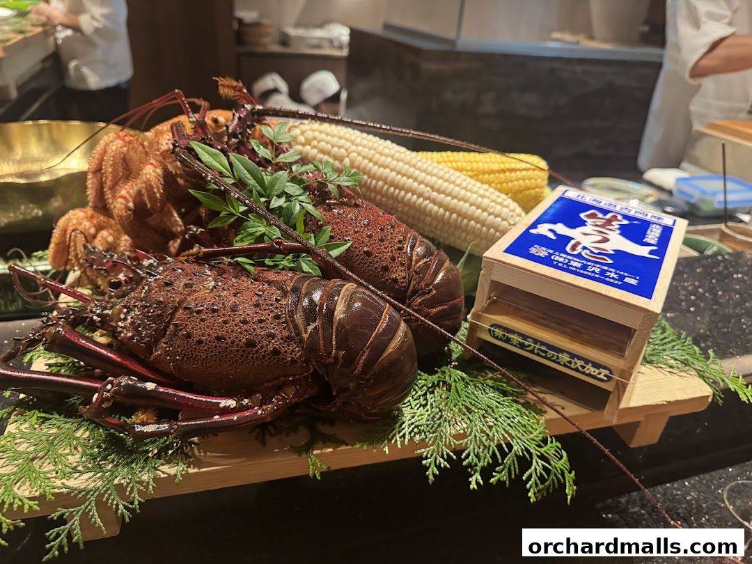 Fresh lobsters and corn displayed on a wooden board with Japanese text.