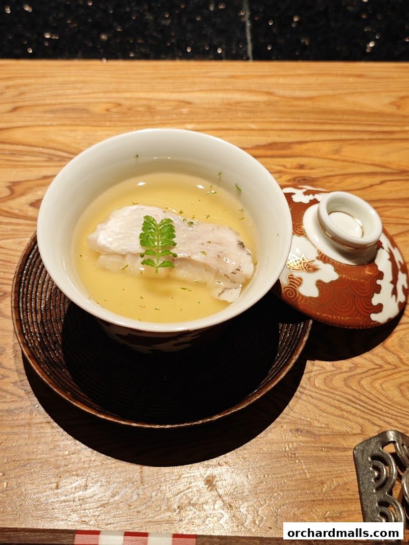 A delicate dish of fish in broth, garnished with a sprig of greenery.