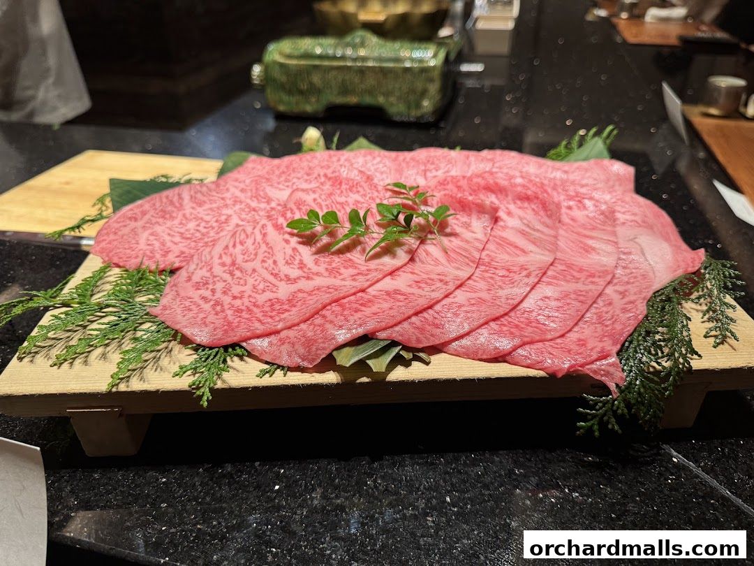 Thinly sliced raw beef with marbling, garnished with greenery on a wooden board.