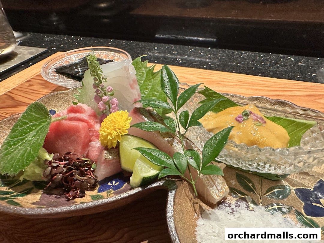 A beautifully presented platter of assorted sashimi, including tuna and uni, garnished with fresh greens and edible flowers.