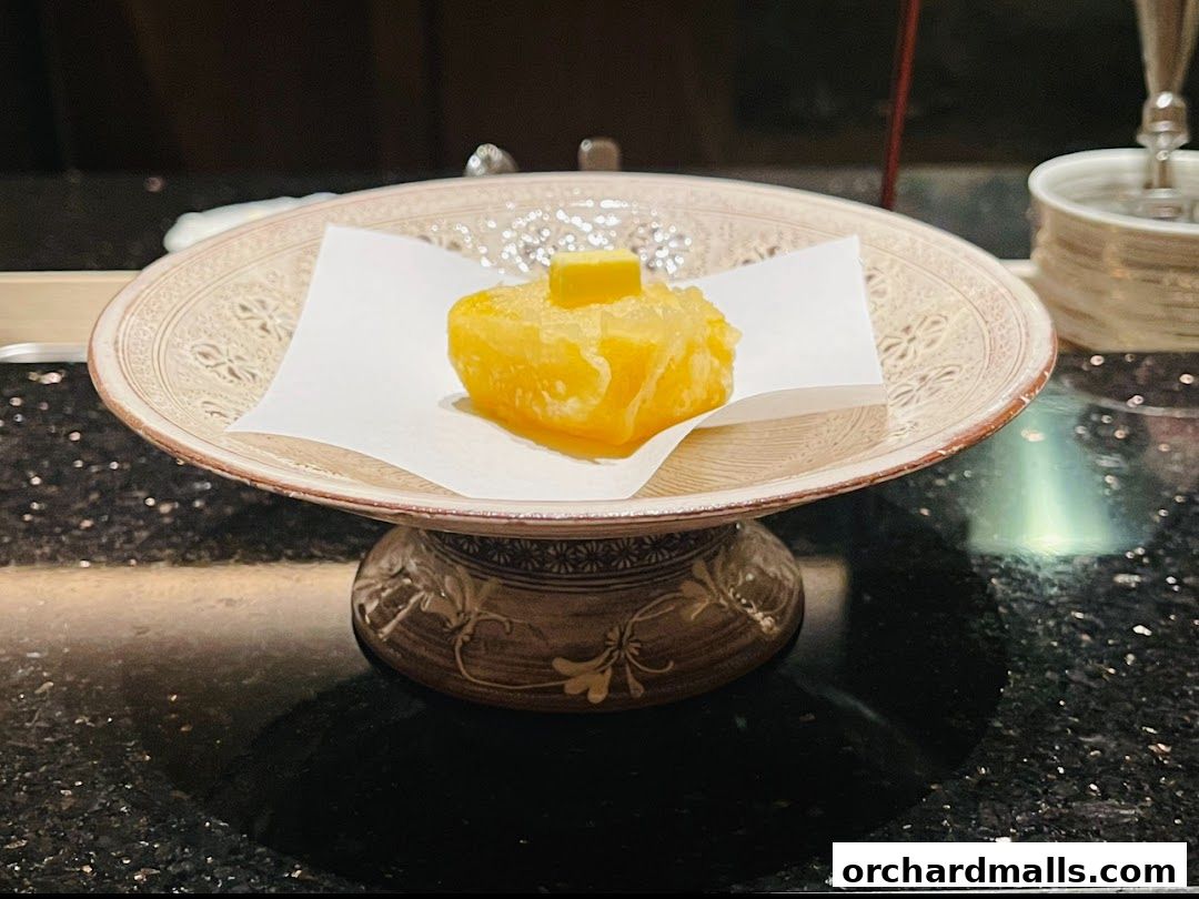 A close-up of a golden dessert with a yellow topping on a decorative plate.