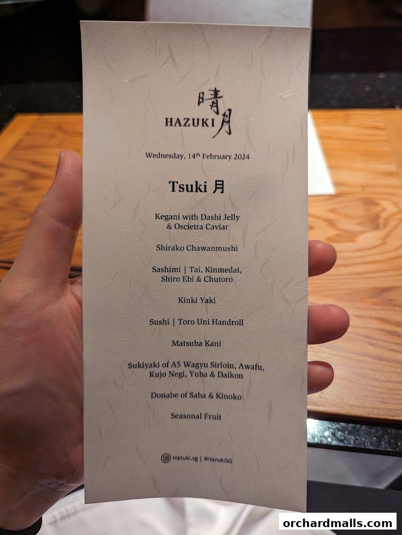 A person holds a menu for Hazuki restaurant featuring a tasting menu called Tsuki.