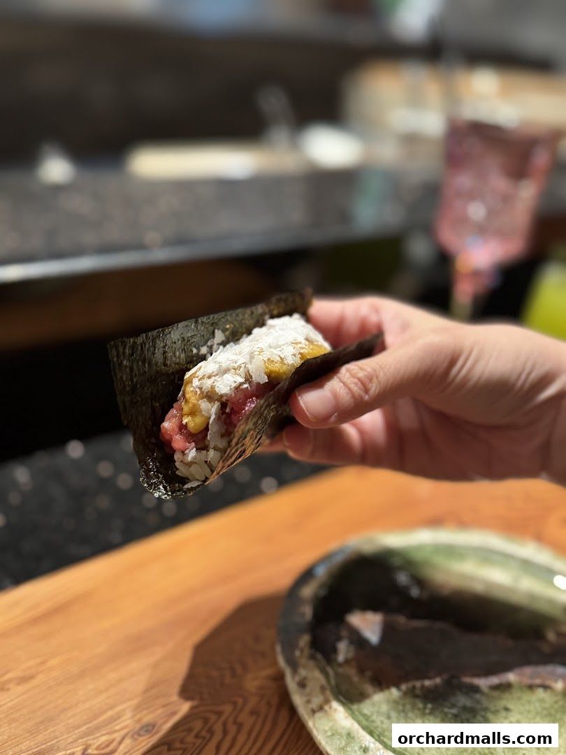 A hand holds a freshly made temaki sushi roll with tuna and rice.