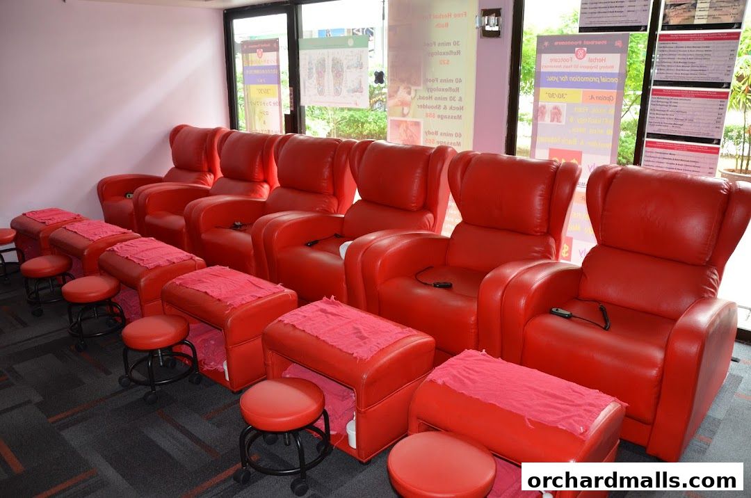 A row of red massage chairs with footrests and stools in a spa.
