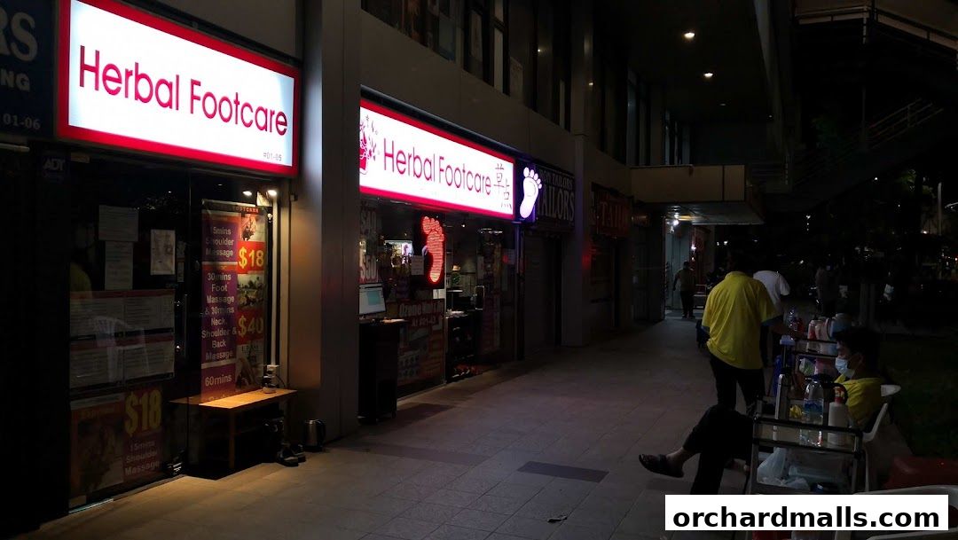 The exterior of Herbal Footcare shop at night, with illuminated signs and service price lists displayed.