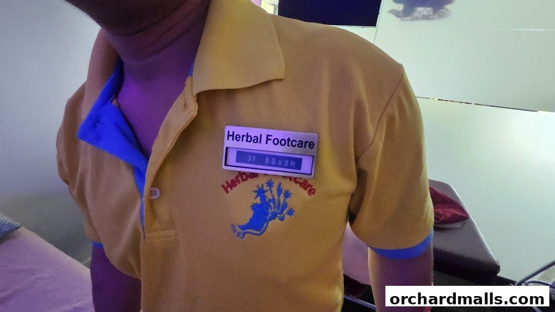 A person wearing a yellow polo shirt with "Herbal Footcare" logo and name tag.