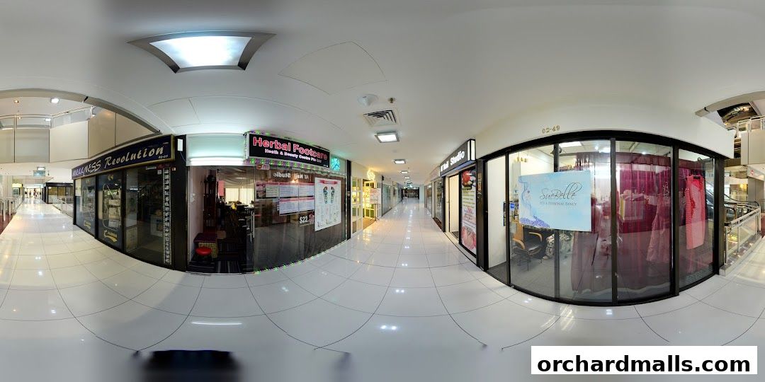 A panoramic view of a shopping mall corridor featuring the Herbal Footcare shop and other retail establishments.