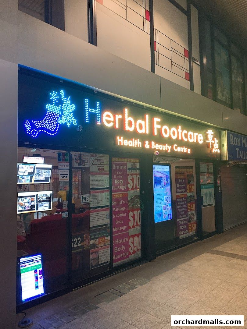 The storefront of Herbal Footcare, a health and beauty center, with illuminated signs and service menus displayed.